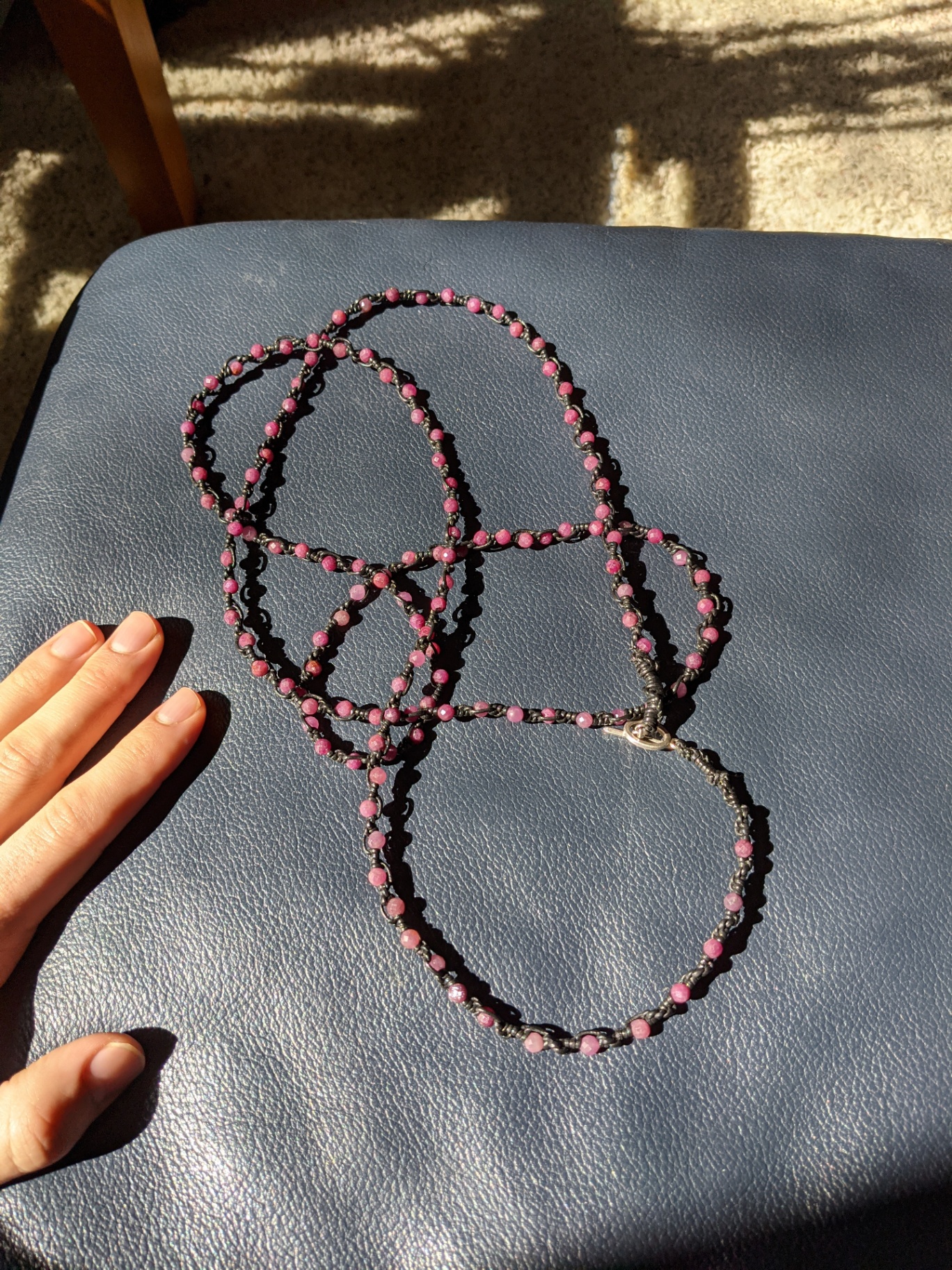 Long ruby-toned macramé bead necklace laid across a dark blue surface in sunlight