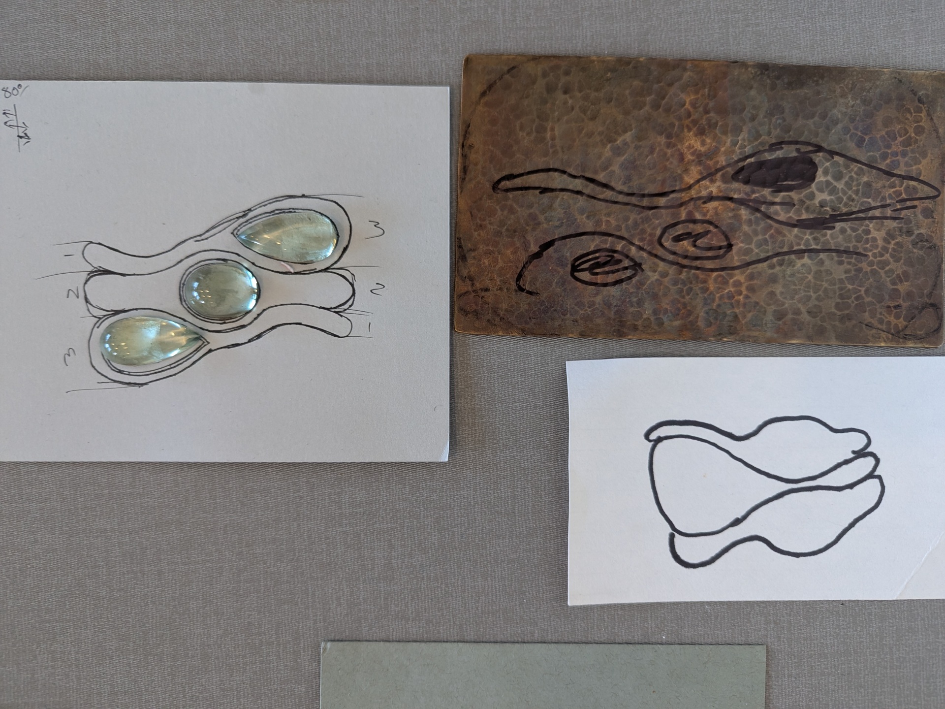 Aquamarine three-stone ring sketch beside a hammered copper plate with ink studies