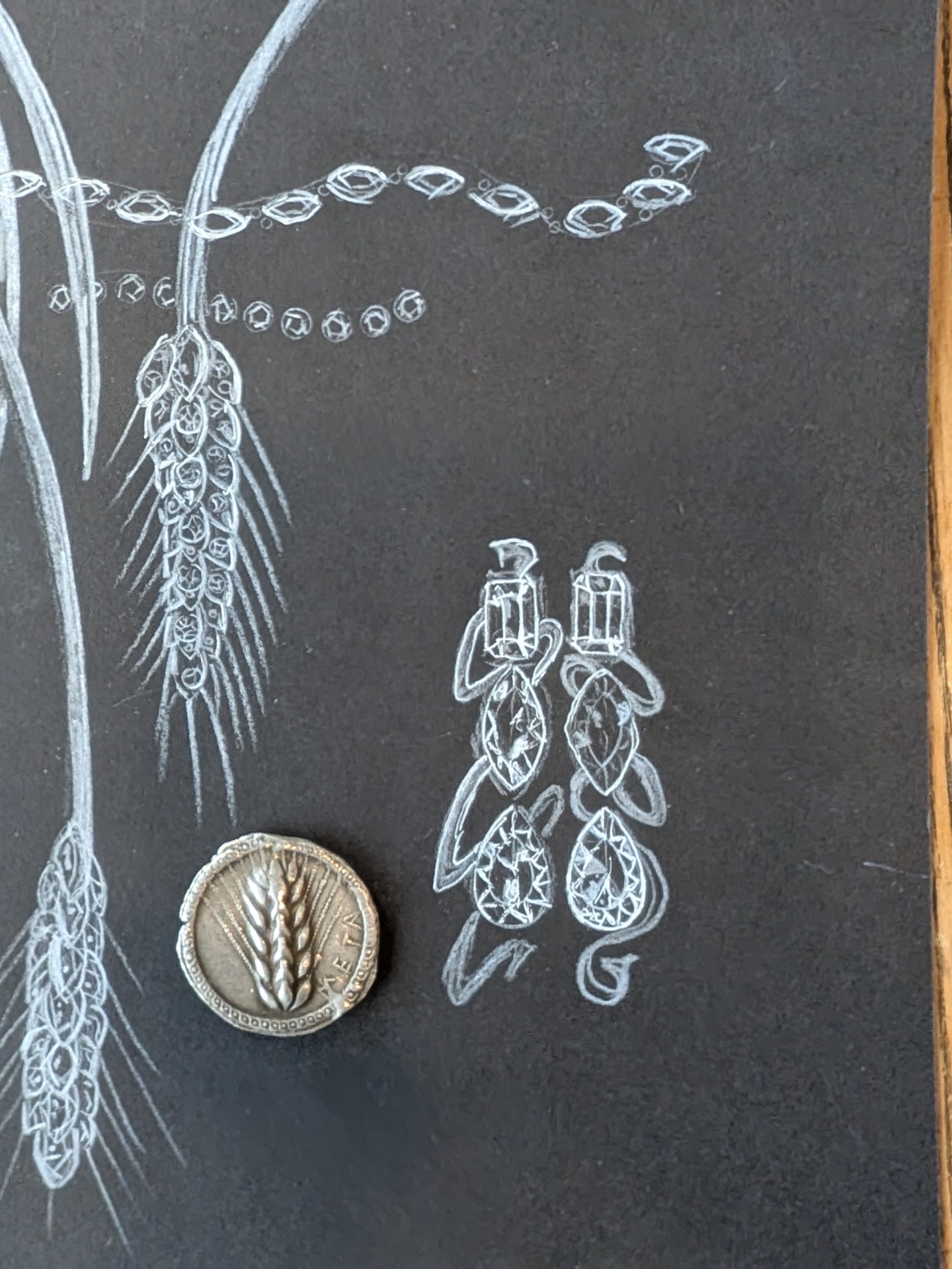 Wheat-and-coin necklace studies in white pencil on black paper, with an ancient silver coin and pavé drop earring sketches