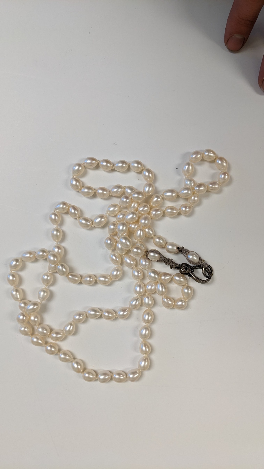 Early pearl necklace with a dark sculptural clasp laid out on white background