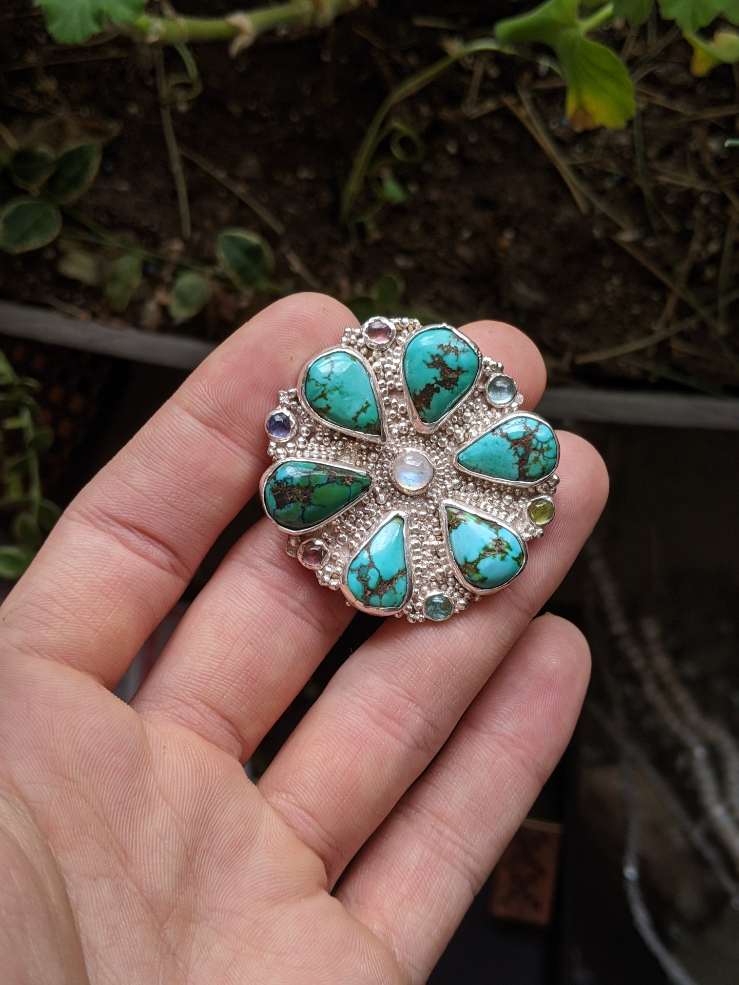 Granulated silver flower ring set with turquoise, moonstone, and accent gems held in hand