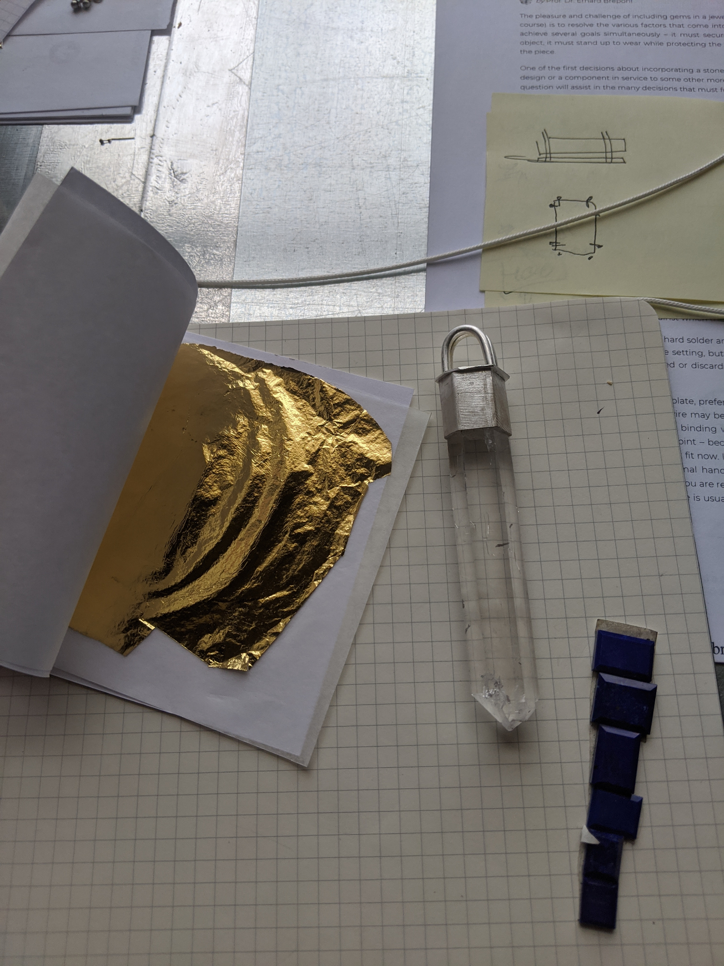 Early process photo showing gold leaf, a crystal point, and hand-drawn bench notes