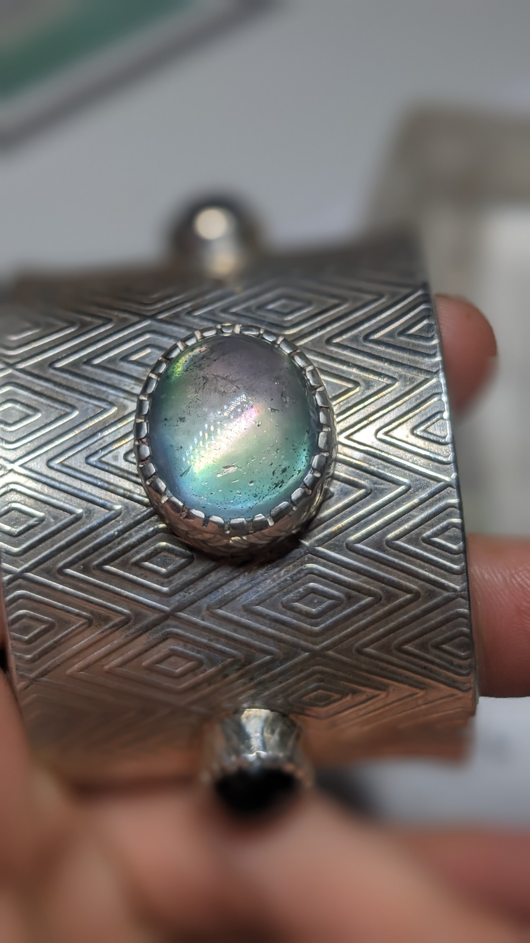 Macro detail of the iridescent opal cabochon set in a serrated bezel on the engraved silver cuff