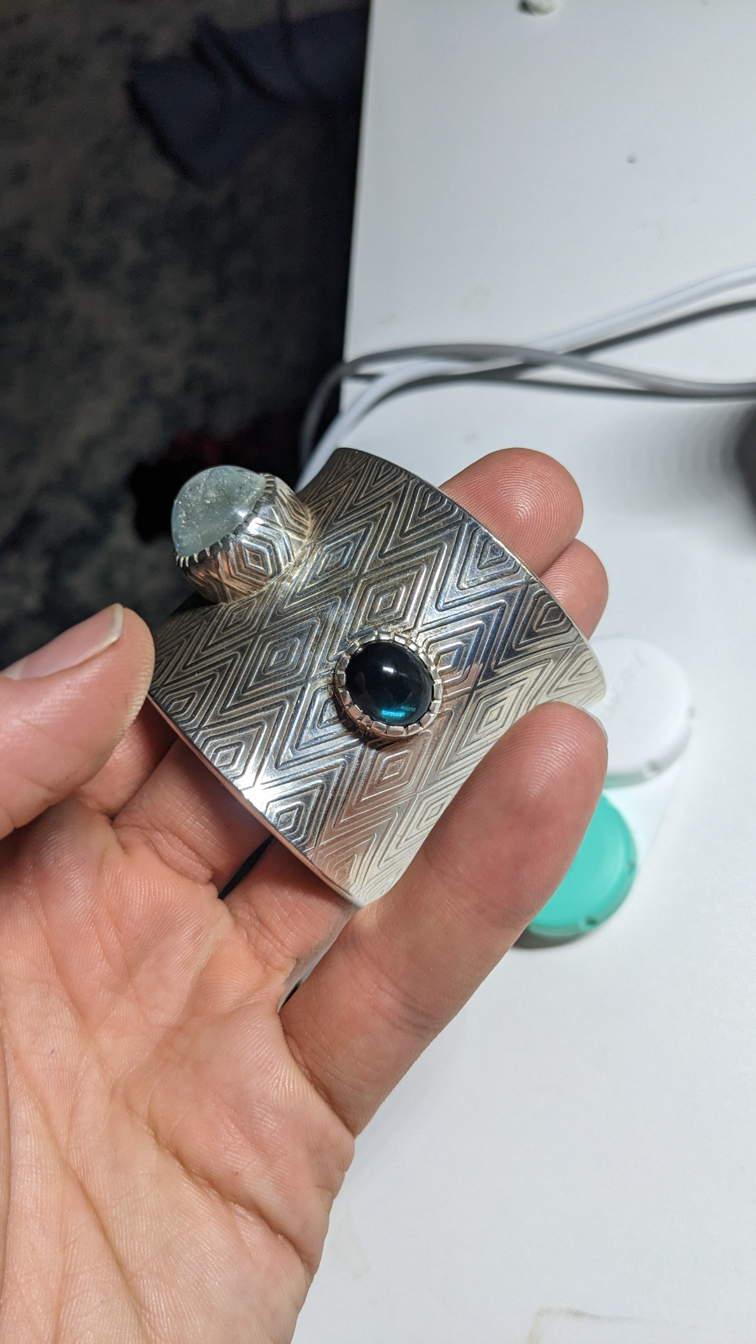 Diamond-patterned silver cuff held in hand showing aquamarine and black onyx cabochons