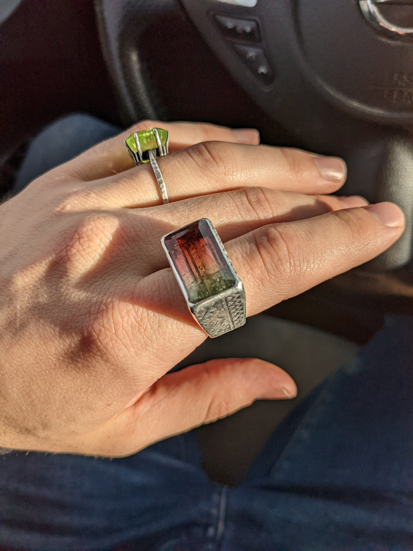Sterling silver engraved signet ring with a watermelon tourmaline center stone, alongside a raw peridot ring