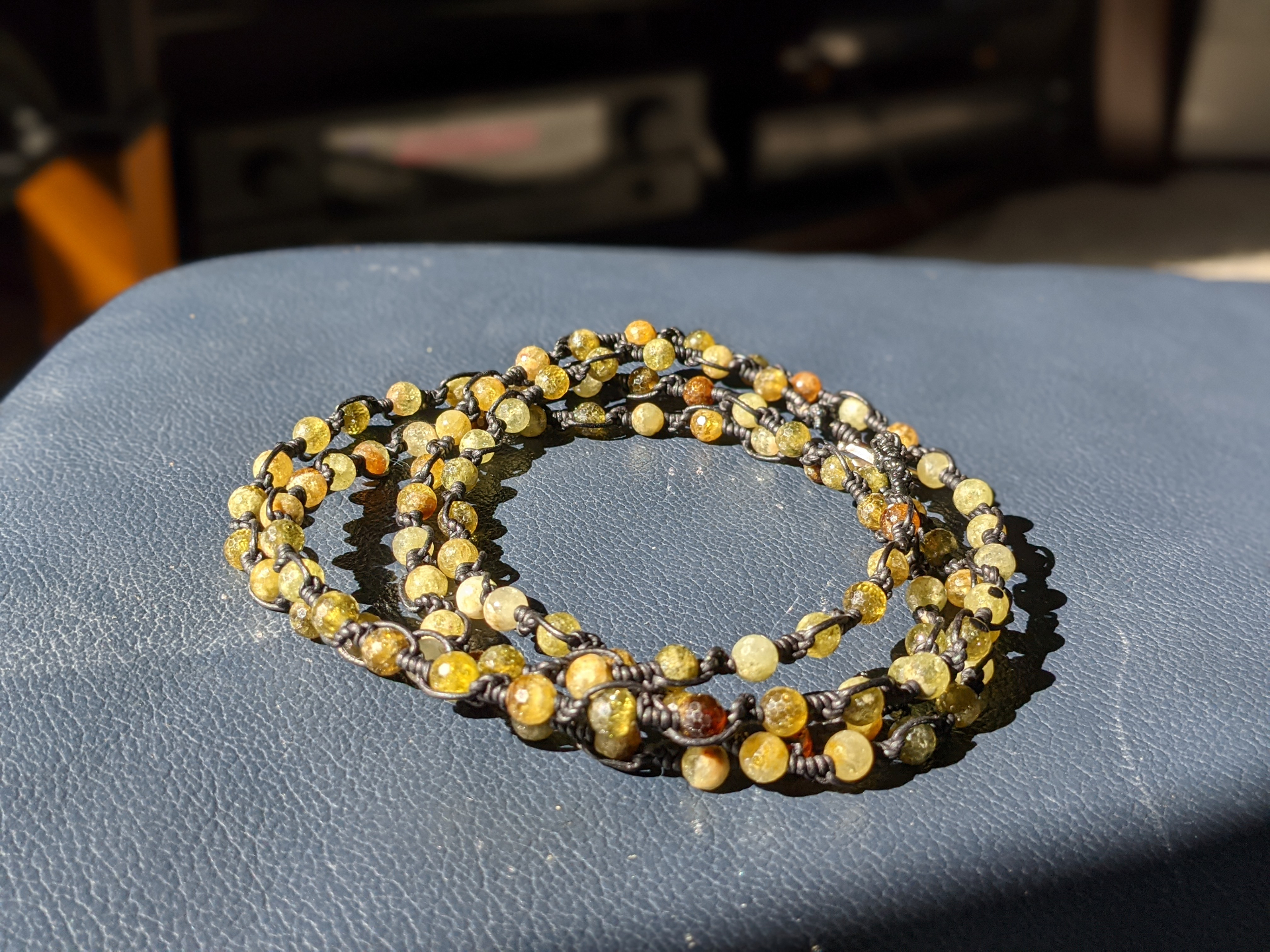 Green garnet wrap-style bead necklace knotted in dark cord on a blue surface