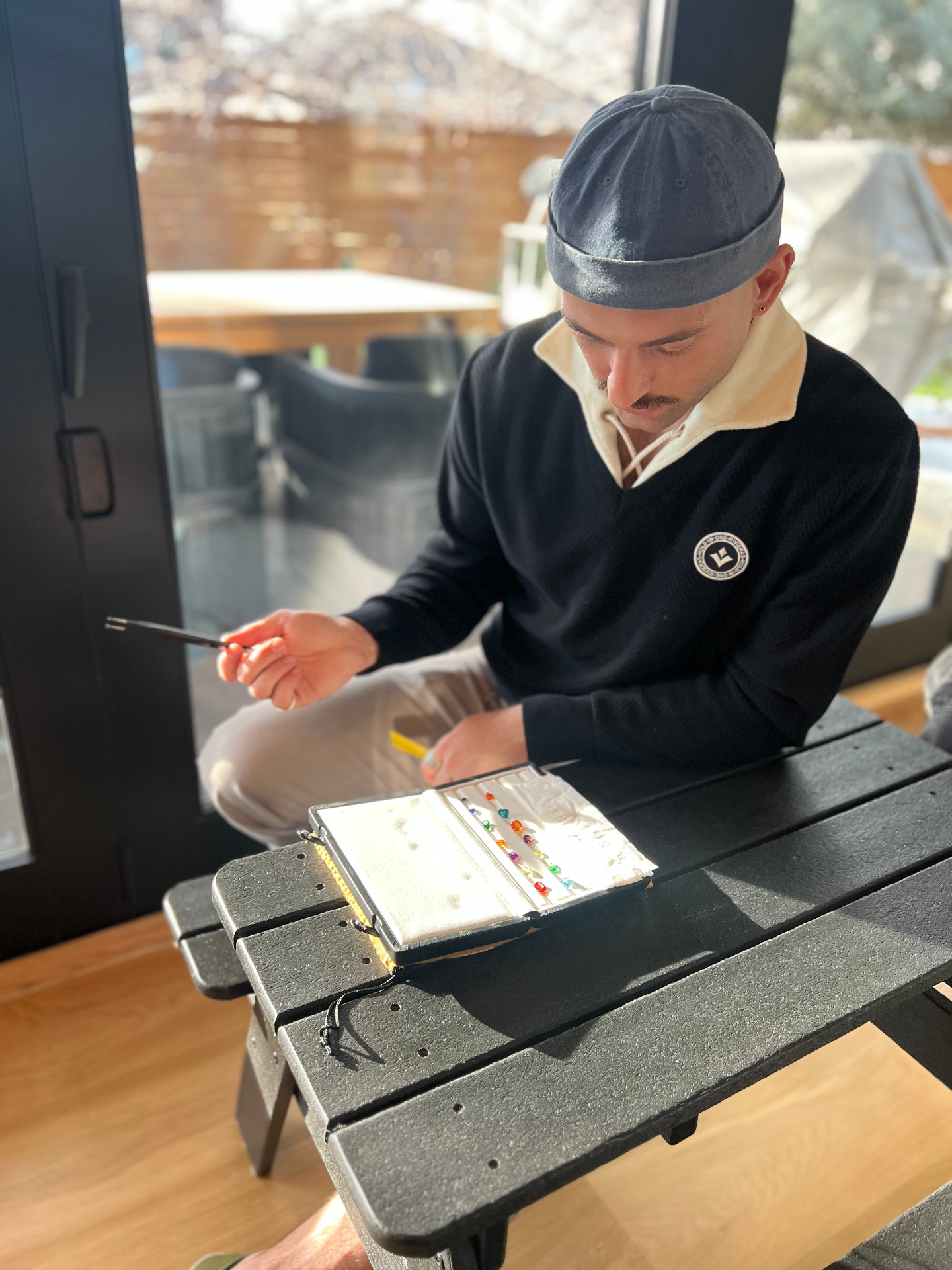 Dayne examining a gemstone tray in bright window light during a sourcing session