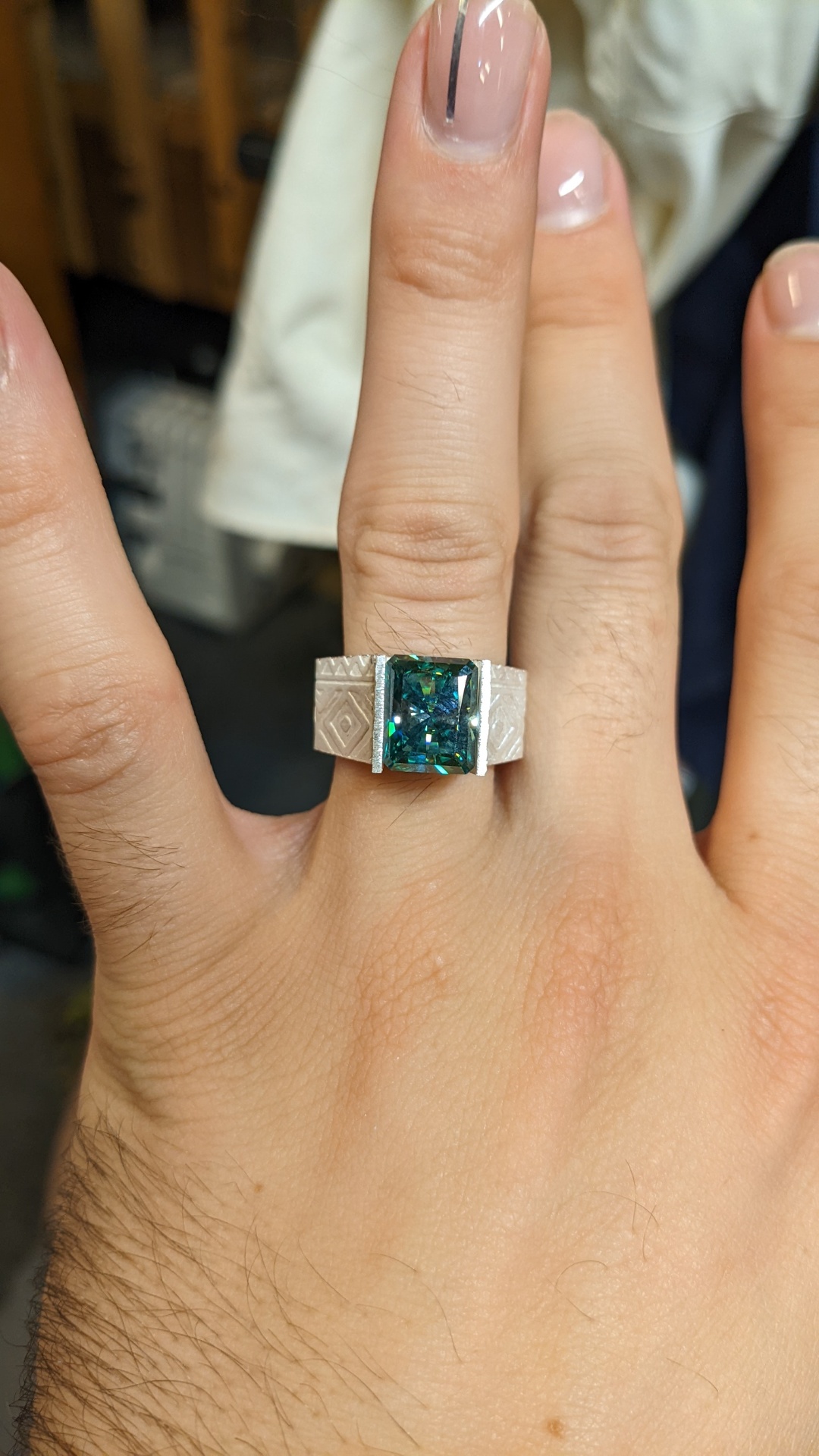 Engraved white gold band with a radiant-cut teal sapphire center stone