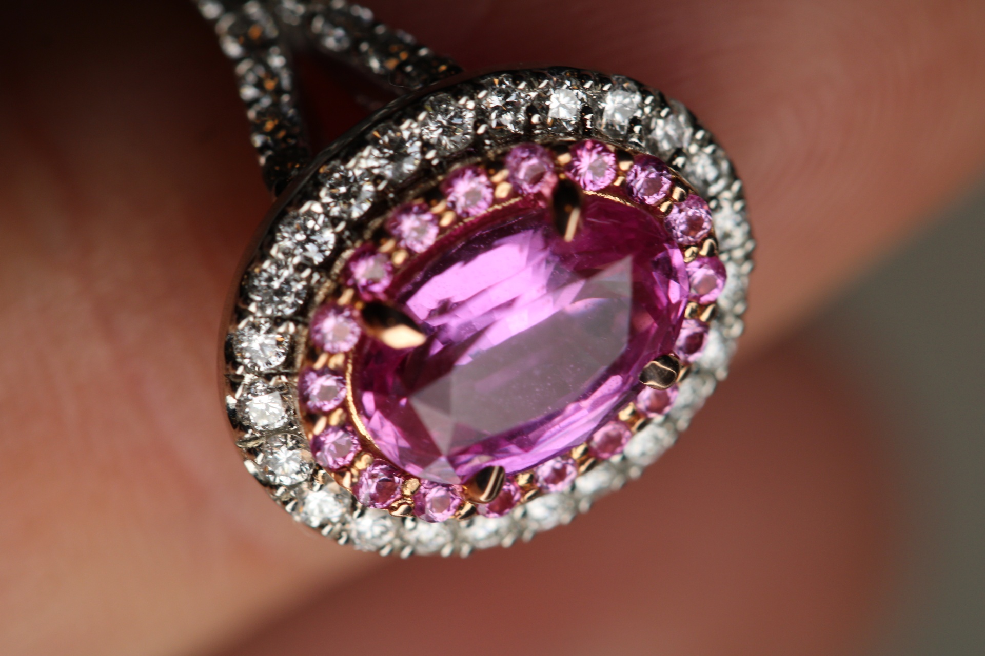 Macro of a pink sapphire oval engagement ring with double halo of diamonds and pink sapphires set in rose and white gold