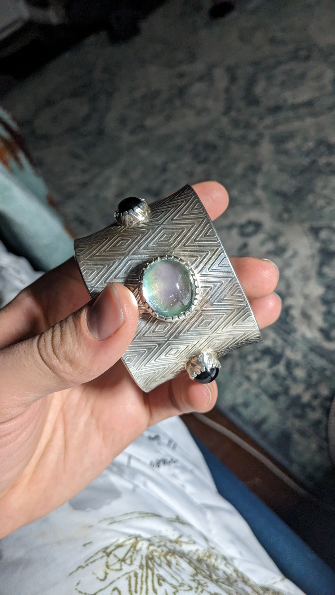 Front view of the diamond-patterned silver cuff featuring a large iridescent opal flanked by black onyx cabochons