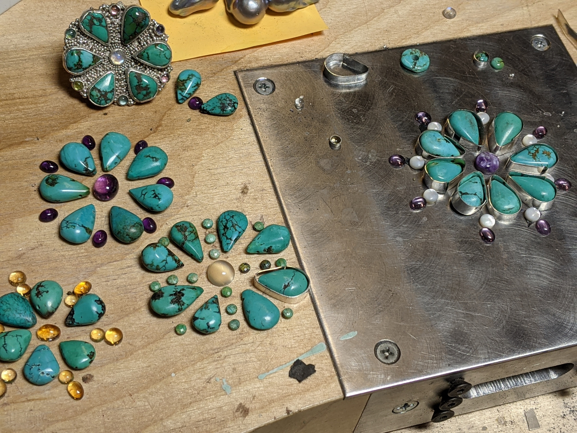 Turquoise and amethyst cabochons laid out in floral patterns on a jeweler's bench