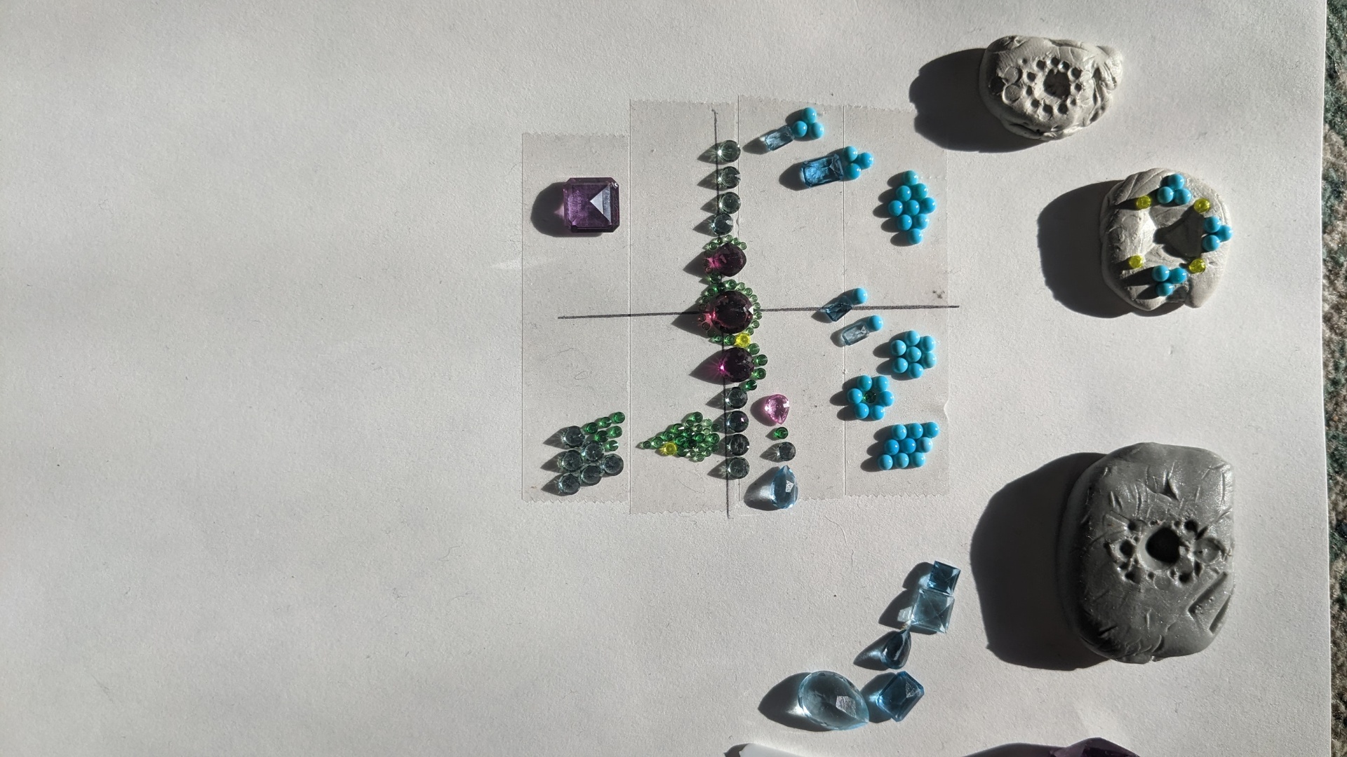 Gem layout study with carved wax forms and arranged colored stones in sunlight